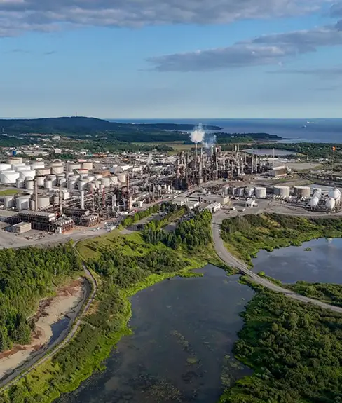 Aerial view of a coastal oil refinery with storage tanks, processing units and surrounding wetlands in Atlantic Canada.