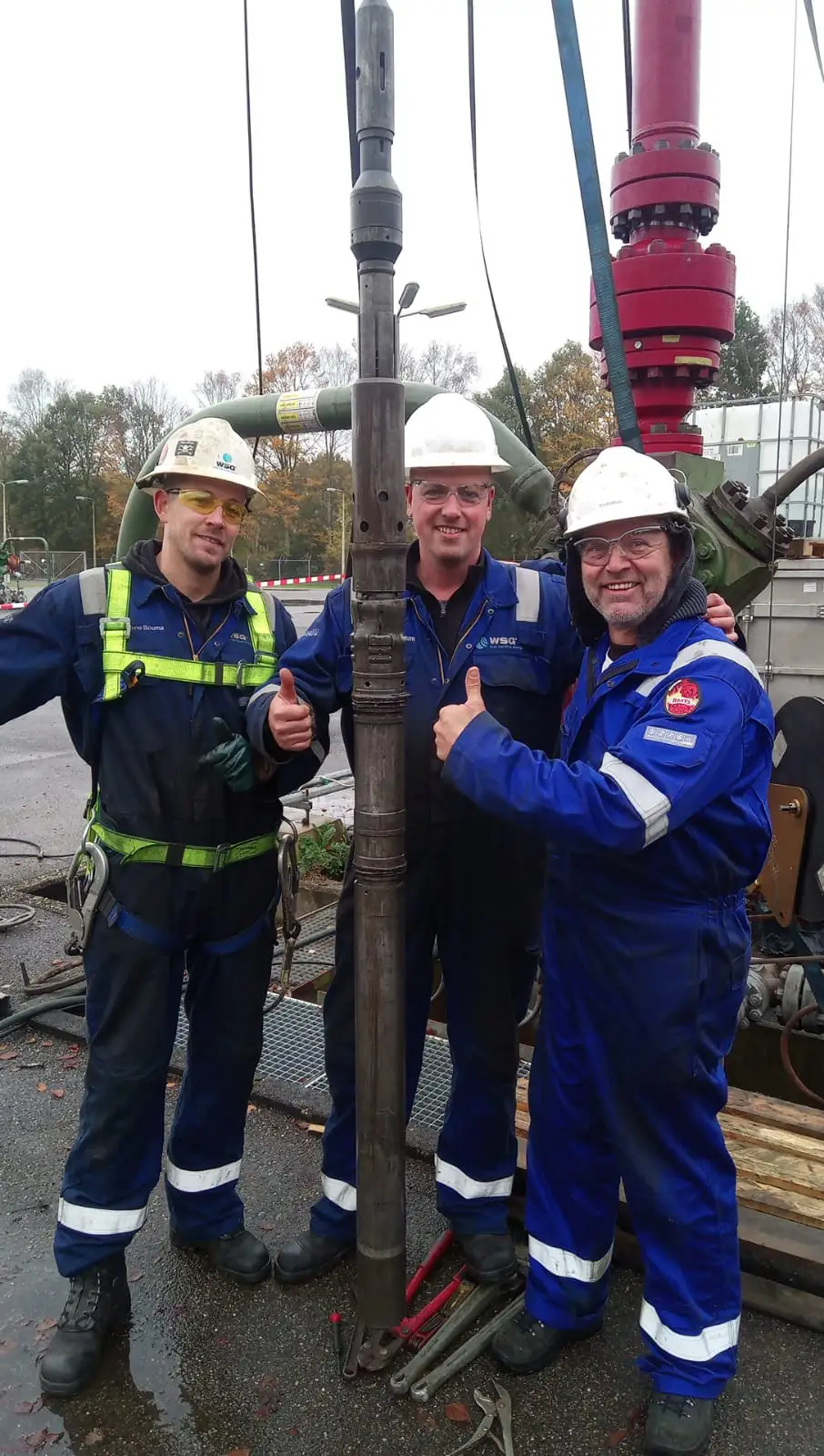 Three oilfield technicians beside a downhole tool during natural gas well service operations.